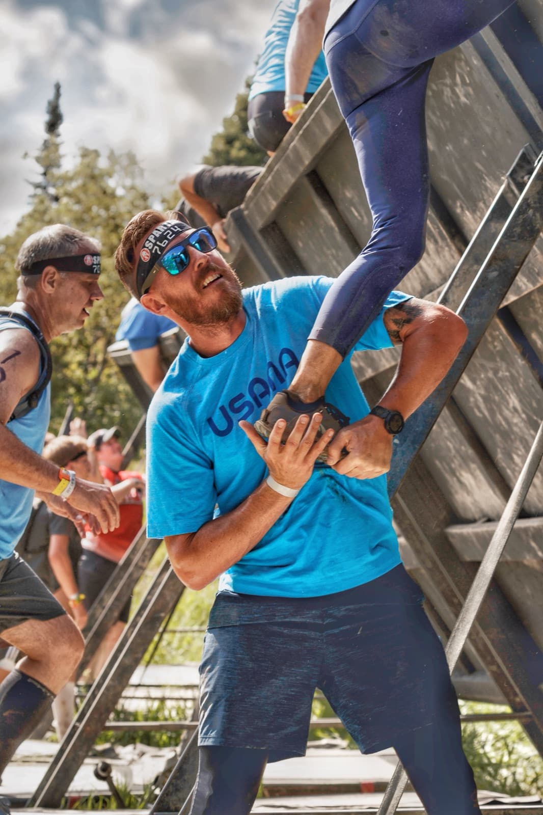 A USANA racer helping a teammate over the A-frame wall